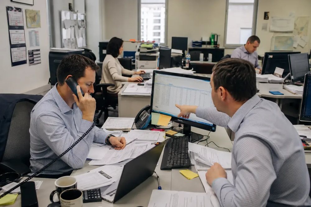 Dwoje pracowników przy biurku w open space, rozmowa telefoniczna i praca na dwóch monitorach