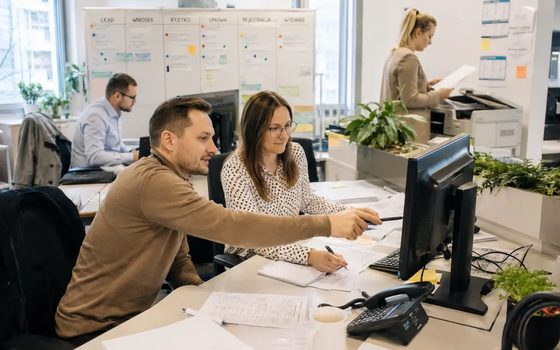 Zespół w biurze, dwie osoby analizują zestawienie na monitorze